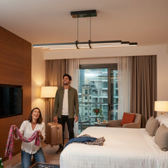 Lüks otel odasında Cosmo Downlight sarkıt avize altında bavullarını hazırlayan mutlu genç çift ve modern aydınlatma atmosferi.