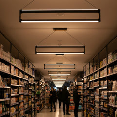 Market koridoru rafları arasında hizada asılı Orion modern lineer LED sarkıt avizelerle homojen aydınlatma.