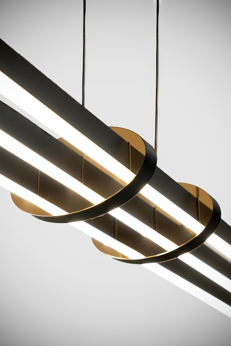Işığı yumuşatan difüzör kapaklı siyah lineer profilleri bir arada tutan altın sarısı şık metal halkalar.