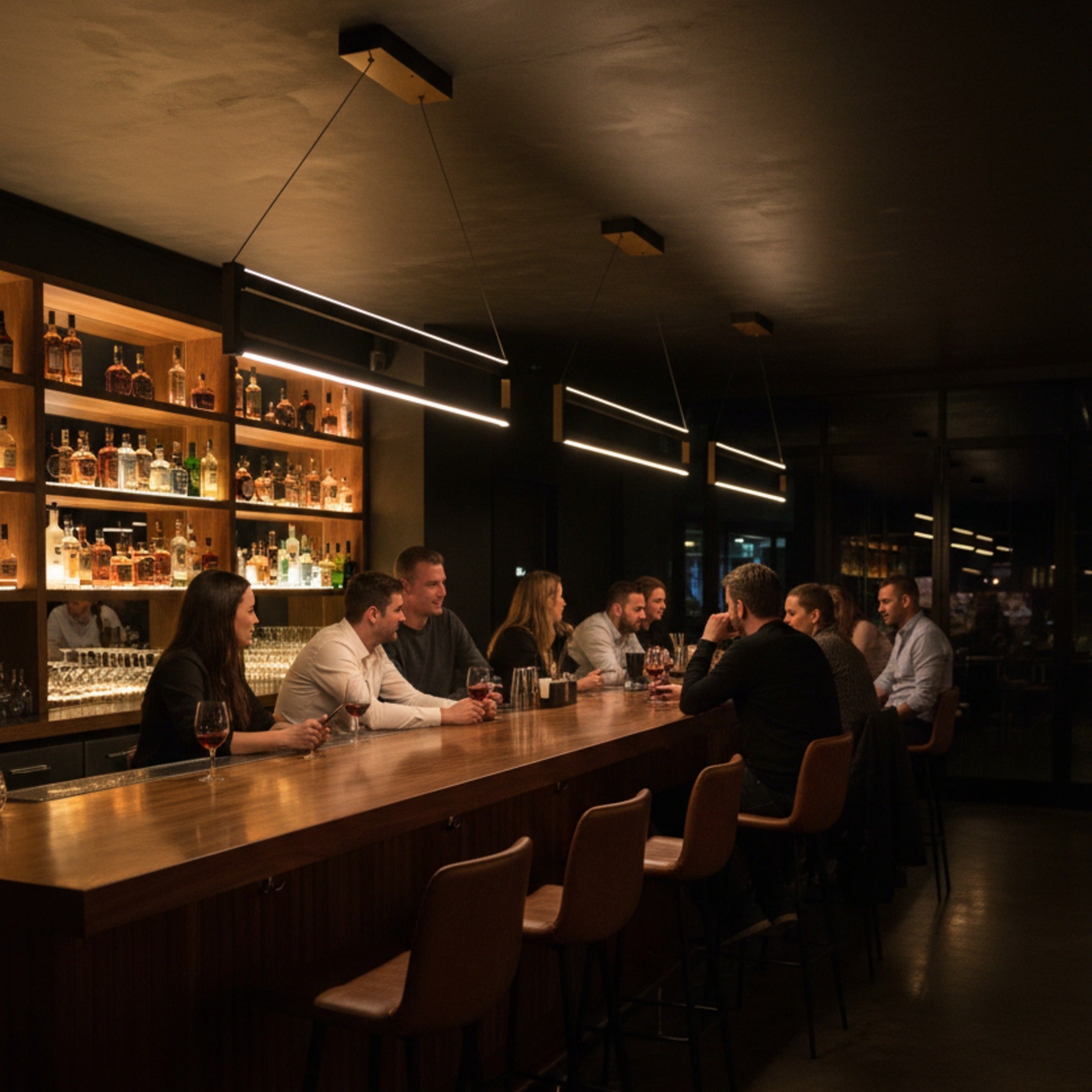Orion modern lineer LED sarkıt avize ile aydınlatılmış şık bir bar tezgahı ve sohbet eden insanlar