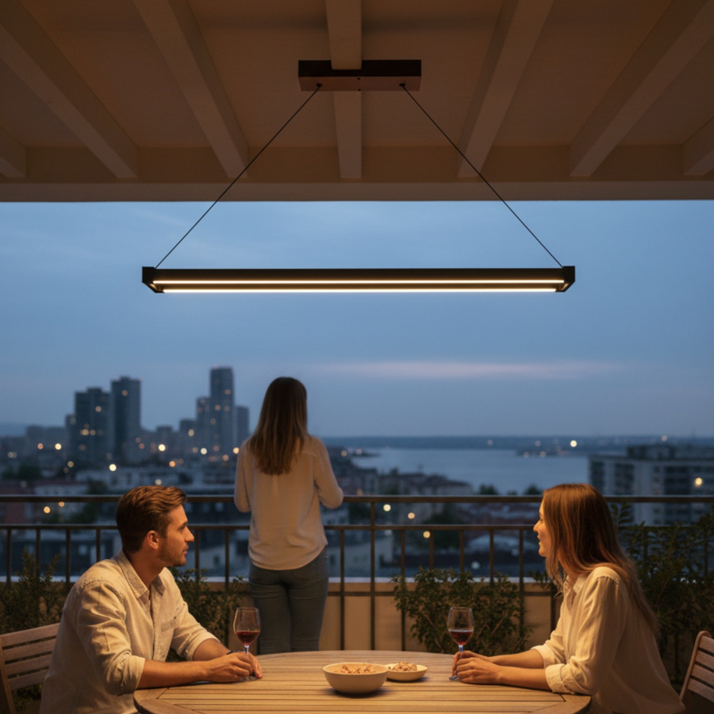 Vega lineer sarkıt balkon aydınlatması altında şehir manzarasına karşı gece keyfi yapan insanlar.